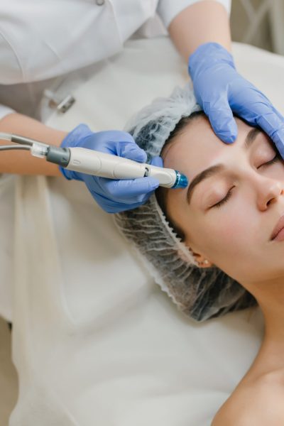 View from above rejuvenation of beautiful woman enjoying cosmetology procedures in beauty salon. Dermatology, hands in blue glows, healthcare, therapy, botox.
